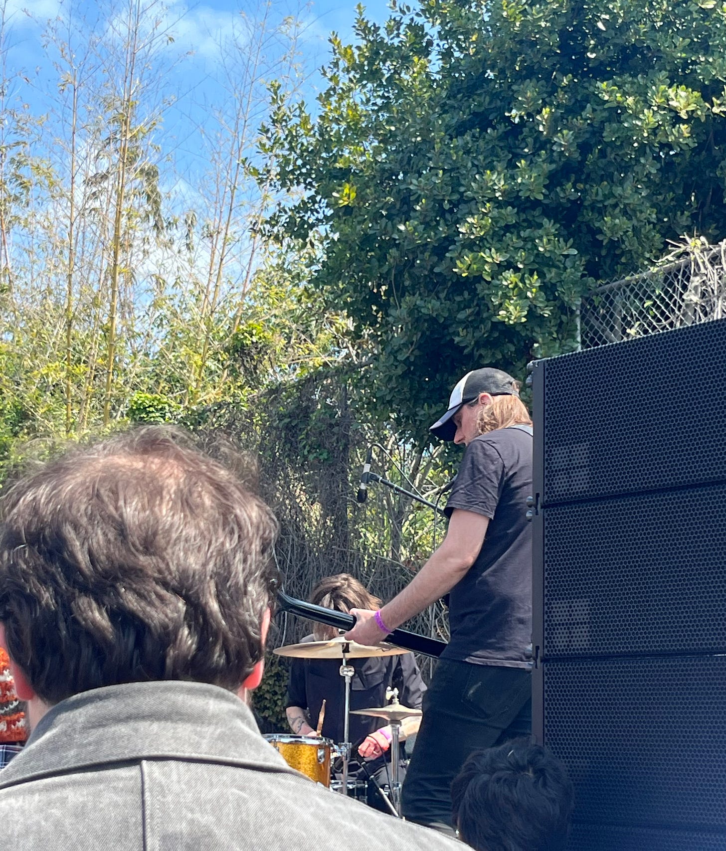 Jeromes Dream playing a show in a climbing gym parking lot in Berkeley. There is an audience member's head in the foreground and a big stack of audio equipment on the righthand side of the photo.