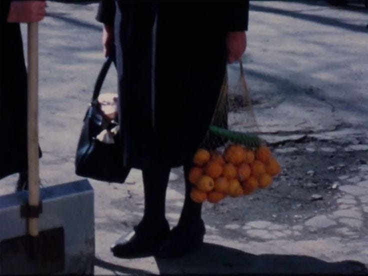This may contain: a person standing on the street with oranges in their hand and luggage behind them