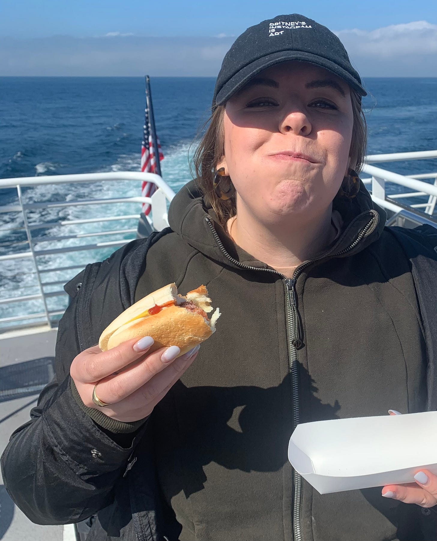 Melissa standing on a boat with her mouth full after taking a bite of a hot dog on a boat