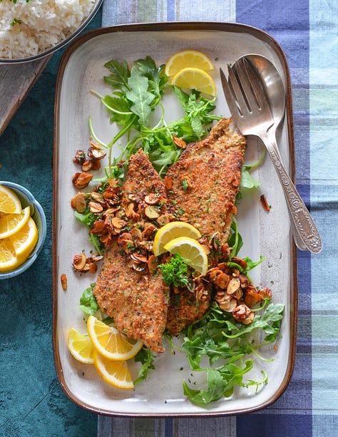 photos of fish almandine on a platter, seafood risotto in a white bowl, Karista pouring a seafood boil onto a plastic tablecloth, Karista holding a whole roasted fish, salmon with brown butter pasta with peas and mint and a crispy fish burger with special sauce sitting on a wooden board