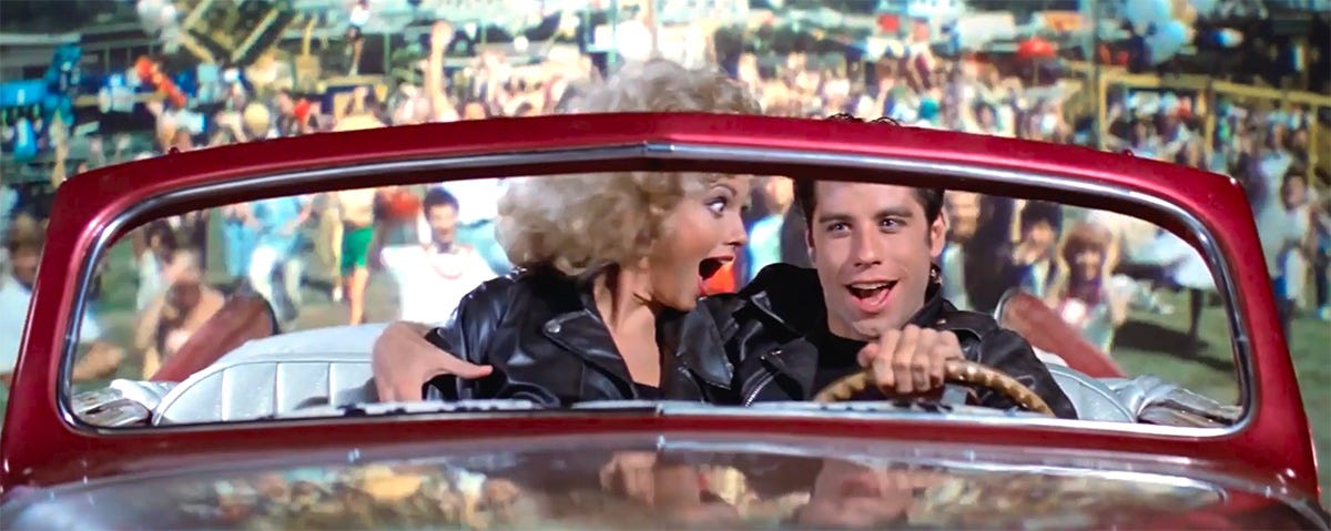 Sandy and Danny are surprised and excited as the car Greased Lightning takes off from the fairground in 1978 film Grease