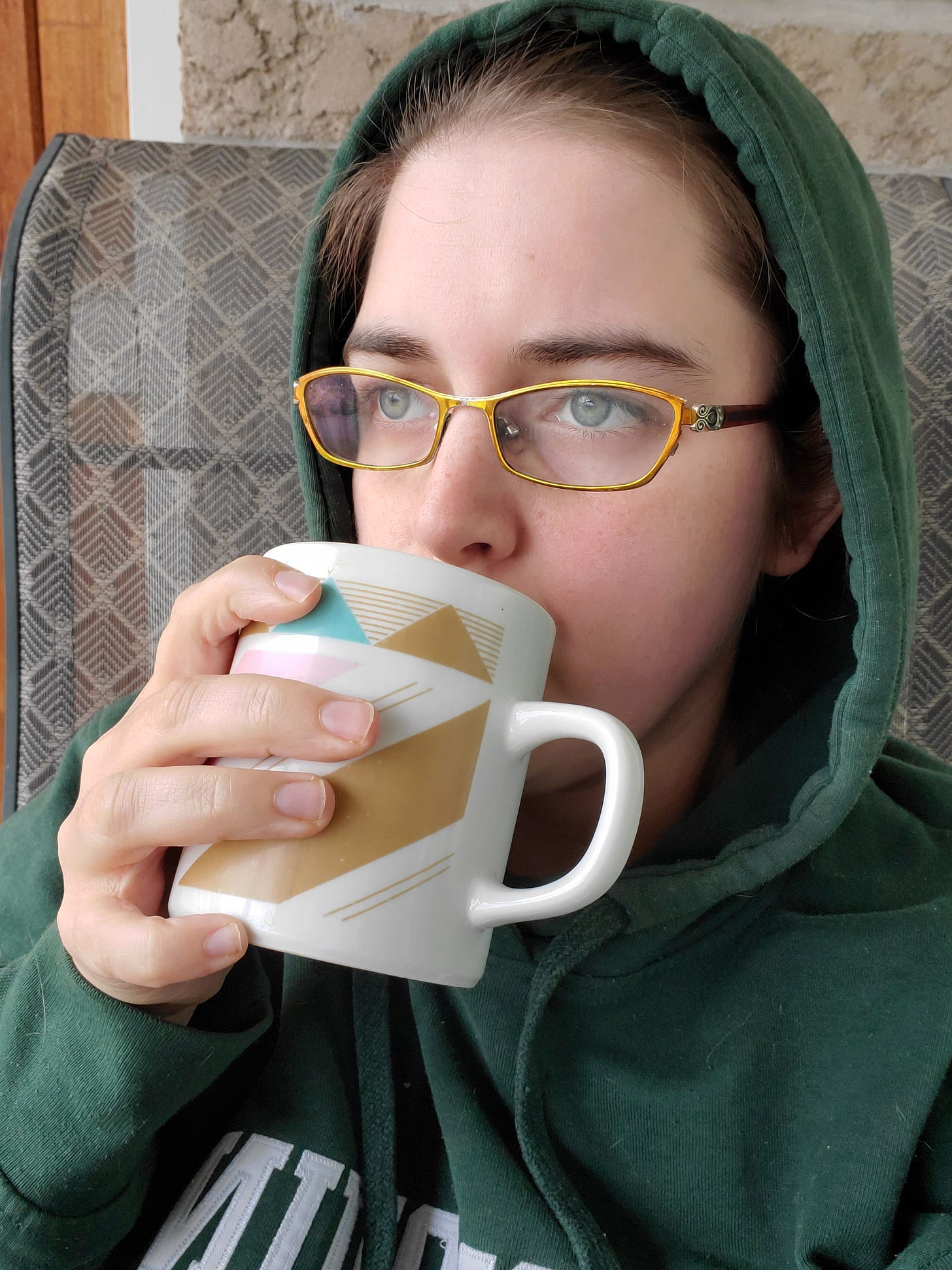 Jerrica stares into the distance sipping from a small mug.