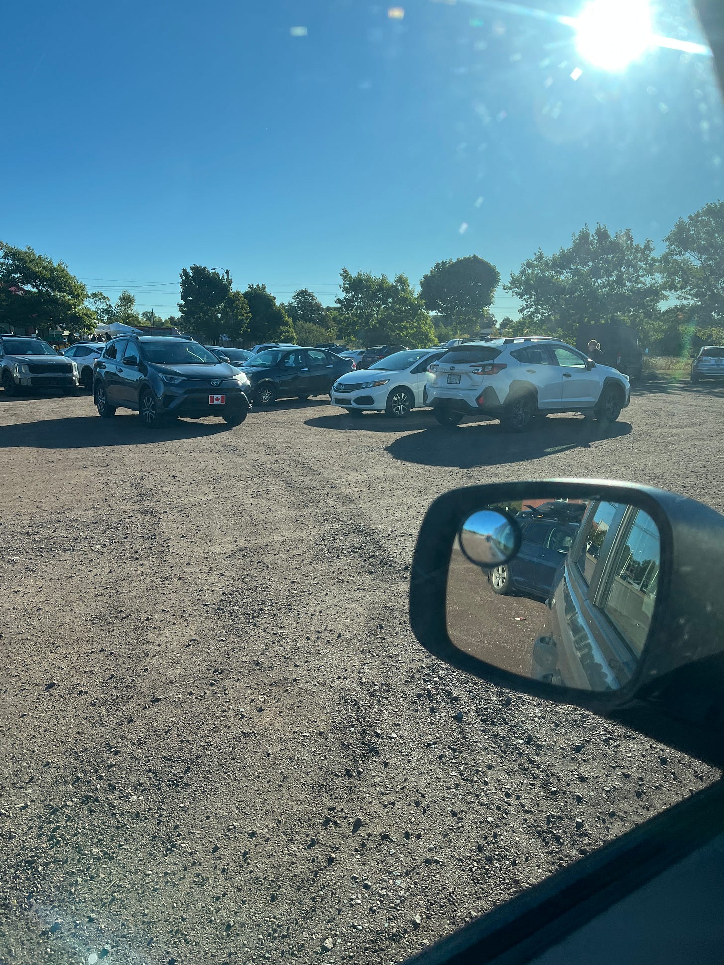 A photo taken from my driver side window of four cars parked in a gravel parking lot. It is parking chaos, with the cars parked against each other coming from different directions.