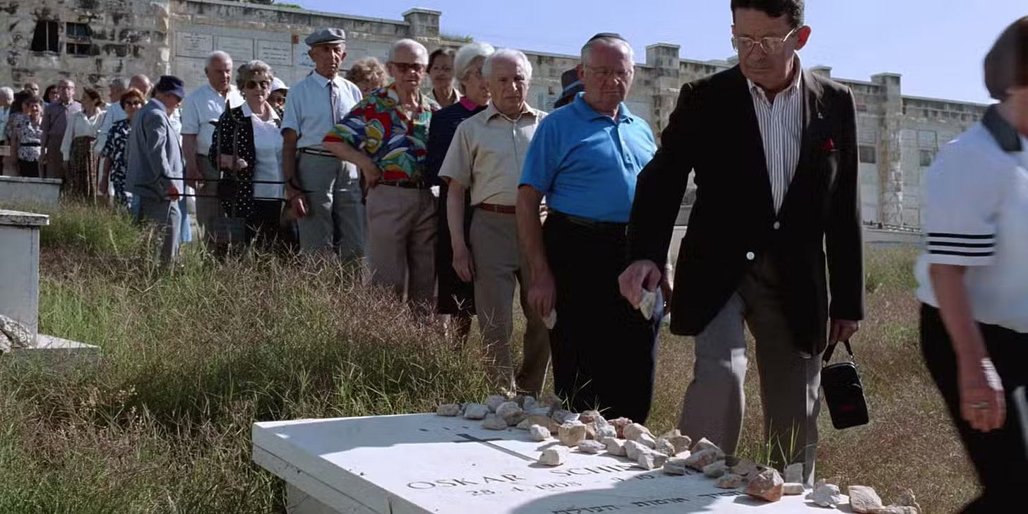 row of mostly elderly people lining up to place rocks on Schindler's grave; image is in color and it's sunny out