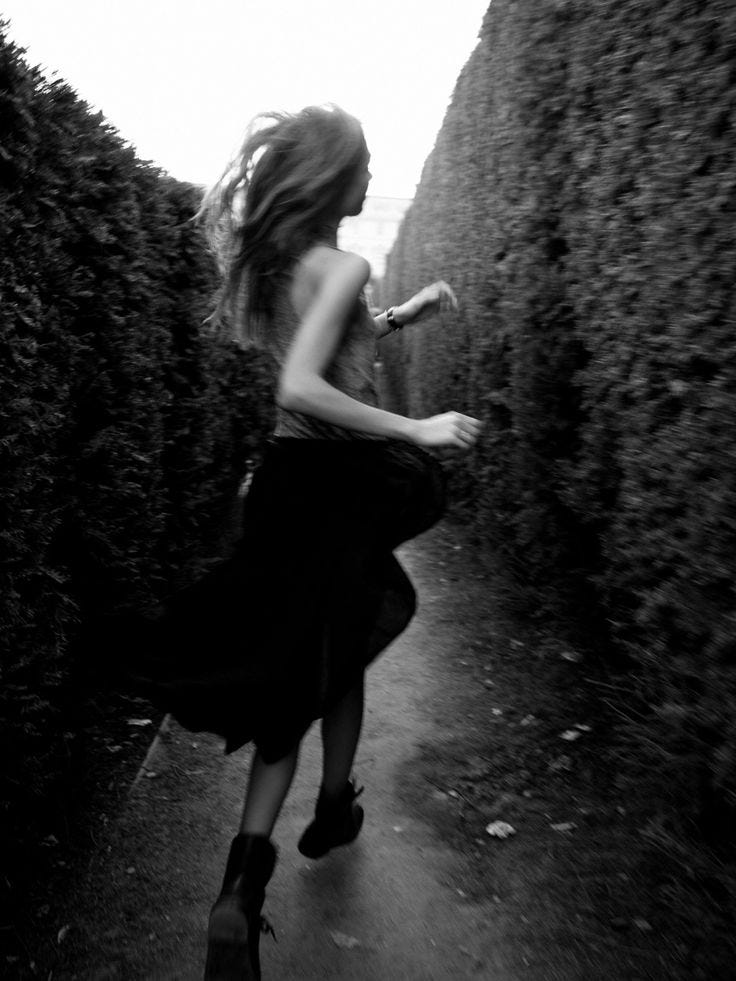 This may contain: a woman is running down a path between two hedges in black and white photo