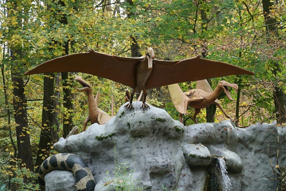 models of flying dinosaurs mounted on a rock in a forest setting.