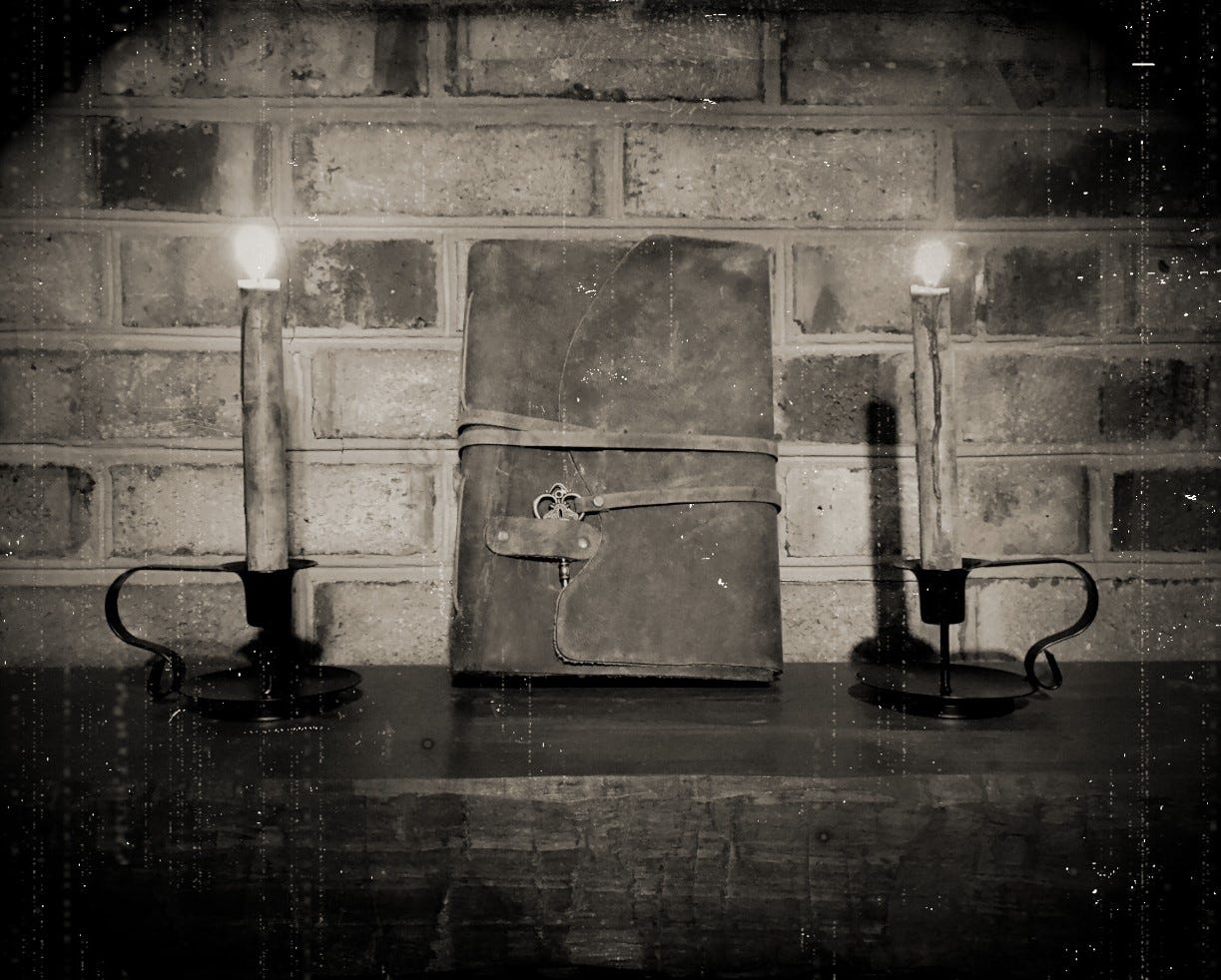 A sepia-toned photo made to look like a Victorian era daguerreotype. The photo shows a leatherbound book on a rough wooden surface with a brick background. On either side of the book is a single lit candle.