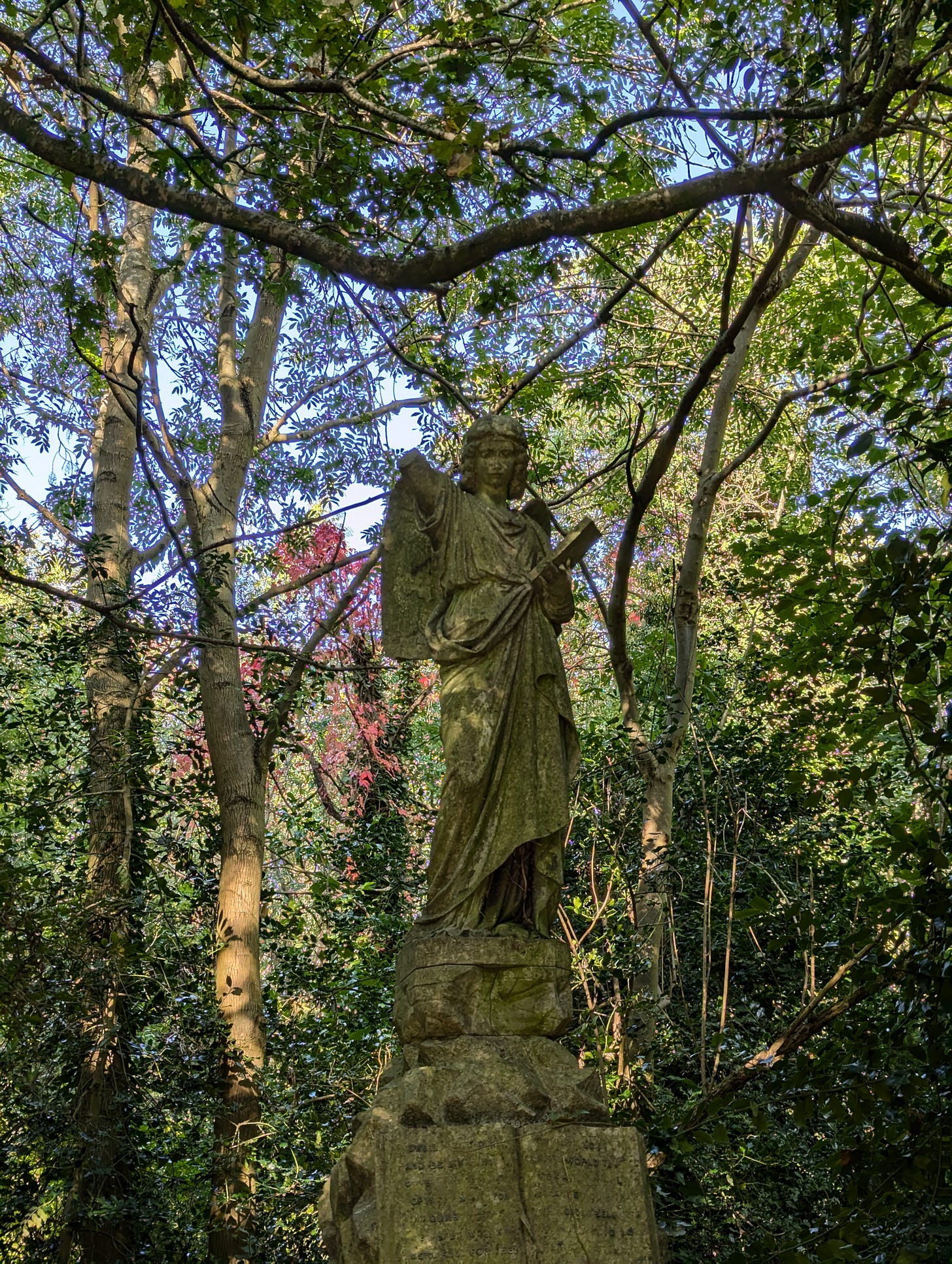An old tomb statue of an angel in Abney Park cemetery, East London, surrounded by trees