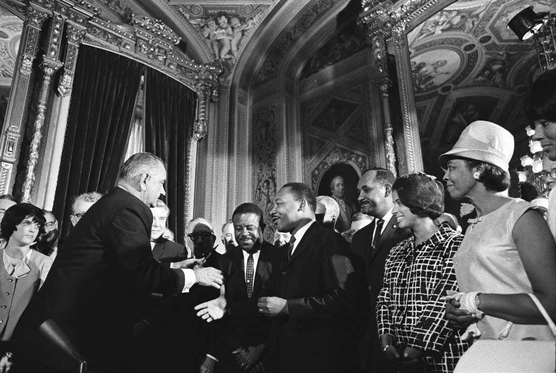President Lyndon B. Johnson extends a hand to shake hands with Martin Luther King Jr. while others watch at the U.S. Capitol in 1965.