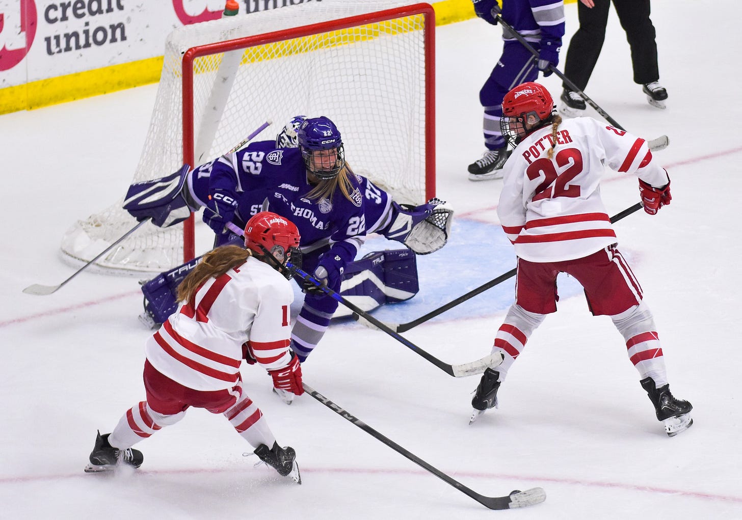 wisconsin women's hockey forward Cassie Hall with a puck on her stick shooting around a St. Thomas defender and Wisconsin's Laney Potter