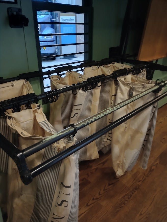 Photo of man in early 20th century sorting mail on train, mailbags and slots on mail train carriage in museum. Mail catcher used by moving train