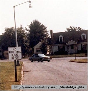 a suburban street with a sign reading "No Wheelchairs beyond this point."