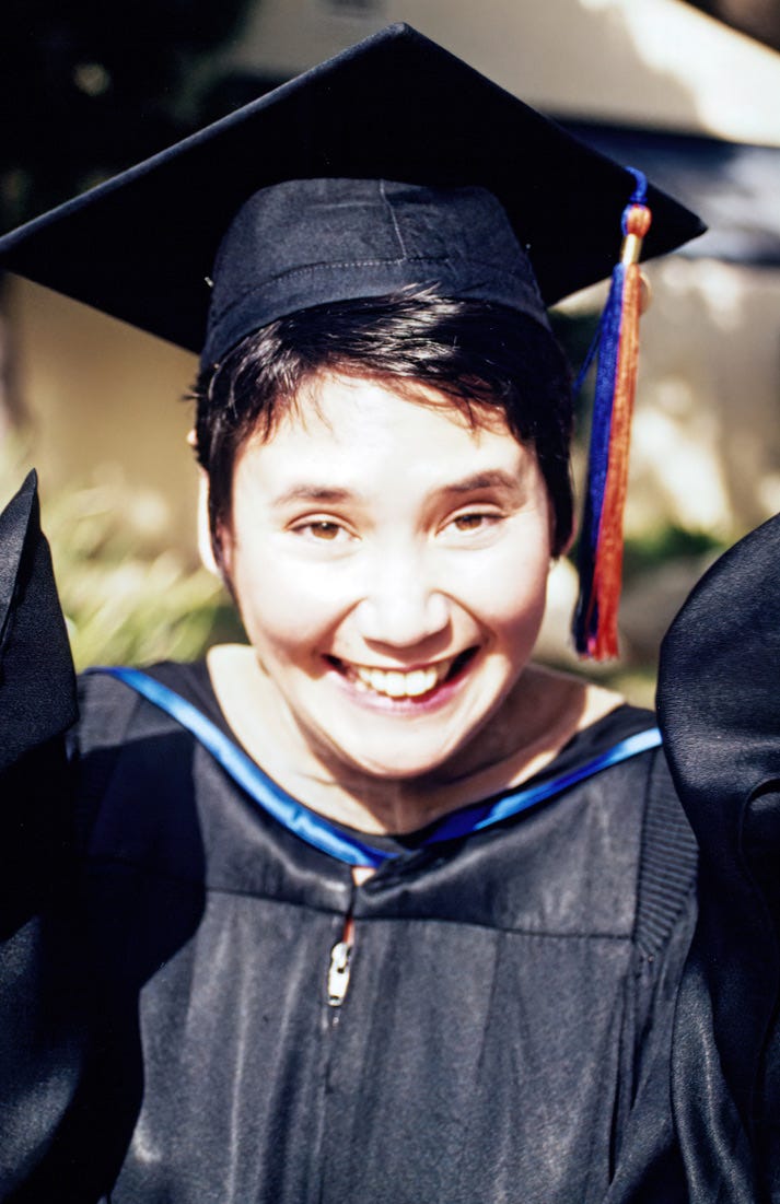 A younger Laverne receiving her MBA. She's smiling and wearing her graduation cap and gown with her arms raised and outstretched in excitement.