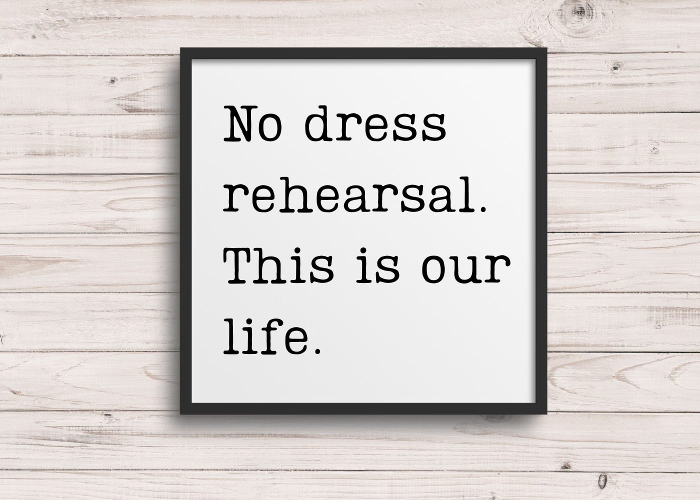 A black frame on a background of whitewashed planks with black lettering on a white background with the words: No dress rehearsal. This is our life.