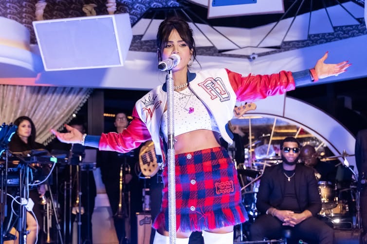 Woman in red and blue plais miniskirt, crop top and leather jacket sings into microphone Woman in red and blue plais miniskirt, crop top and leather jacket sings into microphone