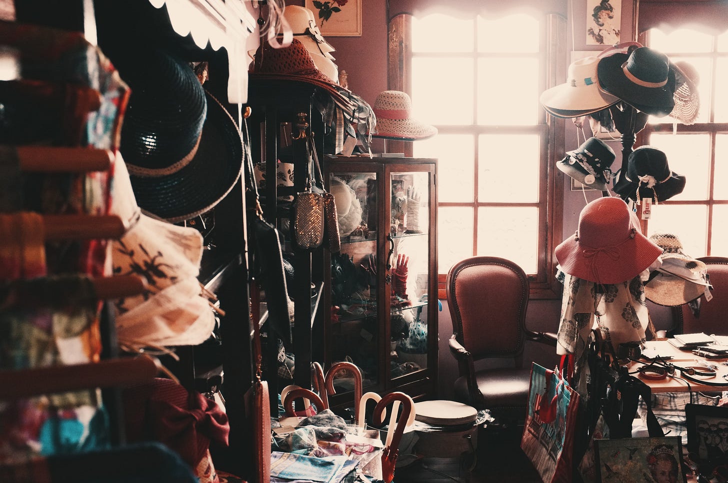 A cluttered corner of a room filled with lady's hats, a chair, a table, a full glass case, an umbrella stand with umbrellas, etc. A cluttered corner of a room filled with lady's hats, a chair, a table, a full glass case, an umbrella stand with umbrellas, etc.