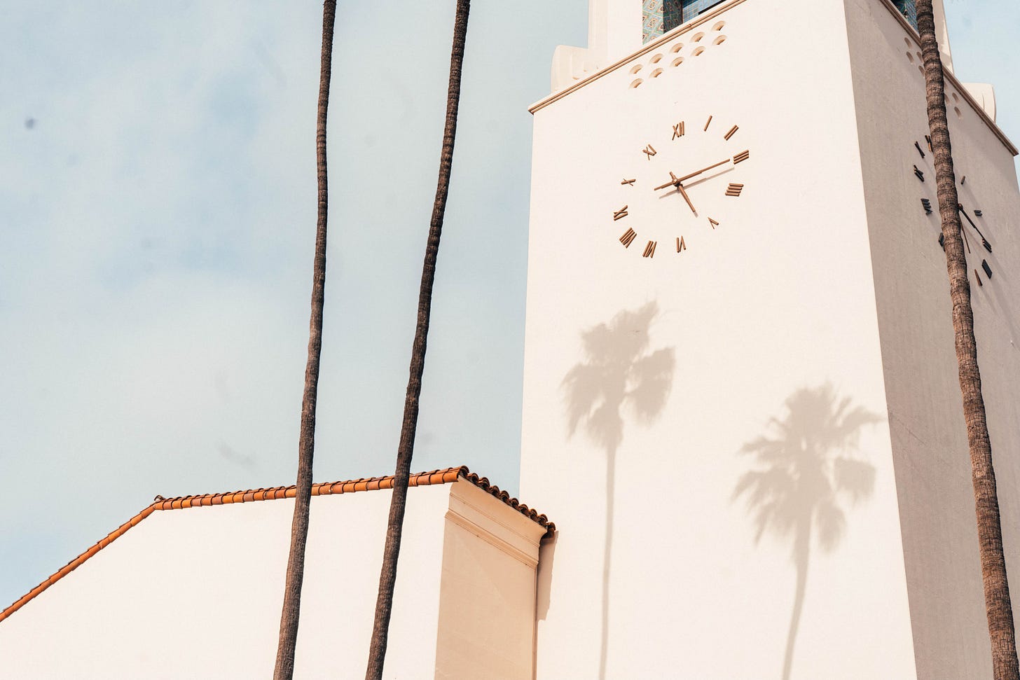 White concrete structure with clock, behind tall skinny trees