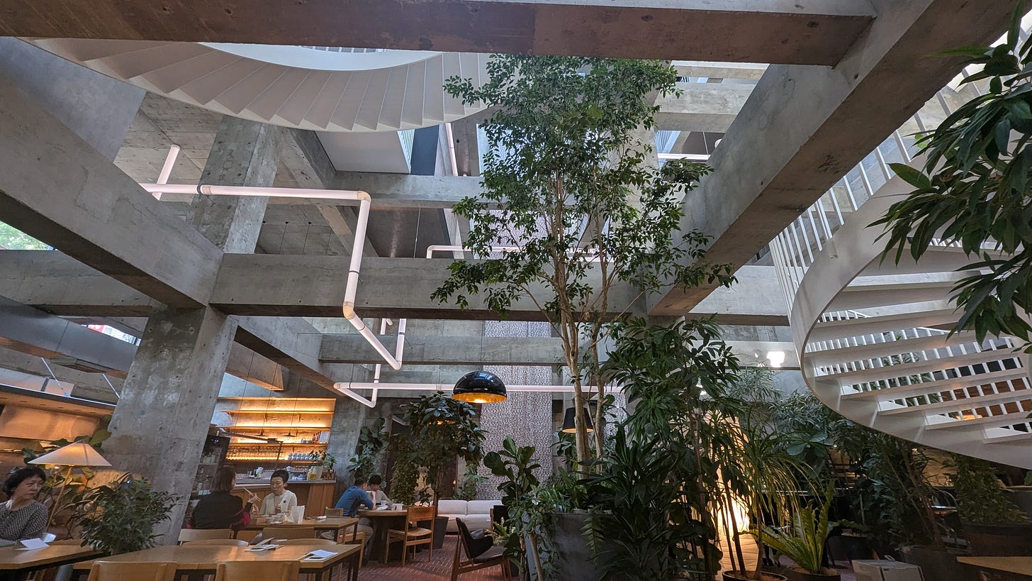 Angular concrete beams and light tubes fill the high ceilings in a space dotted with large trees and stylish seating areas.