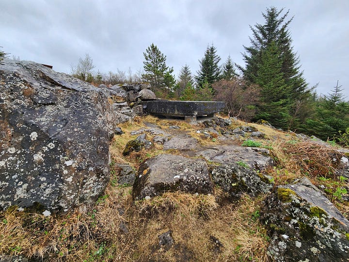 A concrete pillbox bunker on a grassy hillside with lichen-covered boulders and graffiti, and the inside of the pillbox, grey walls with blinding white sunlight through the slits, and boulders left by vandals.