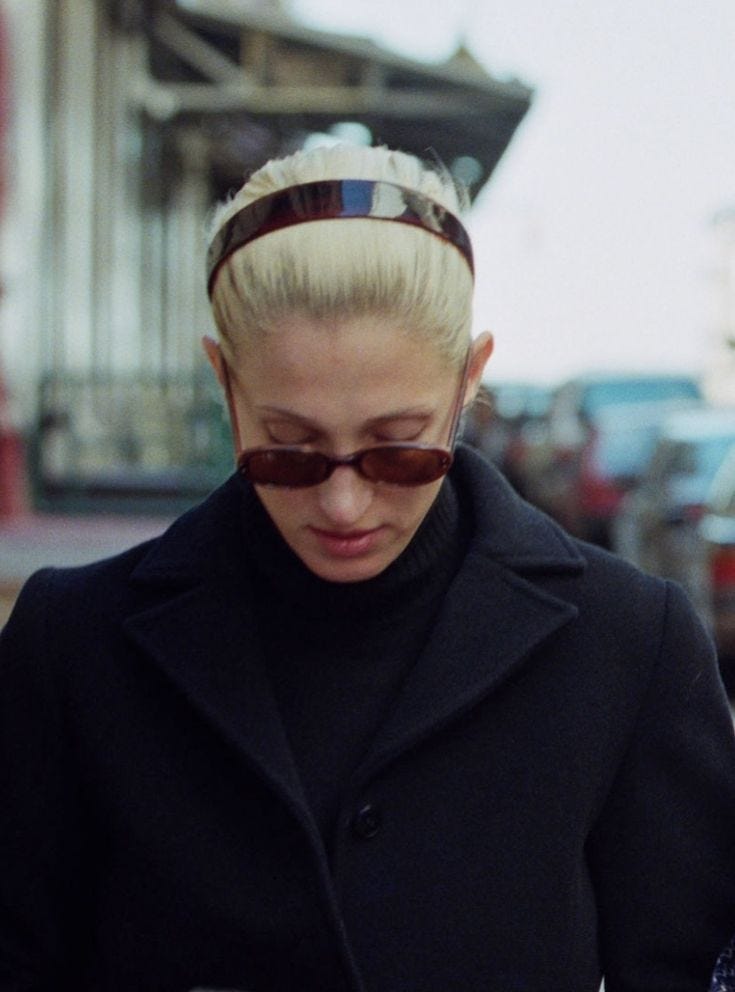 This may contain: a woman with blonde hair and sunglasses looking at her cell phone while walking down the street This may contain: a woman with blonde hair and sunglasses looking at her cell phone while walking down the street