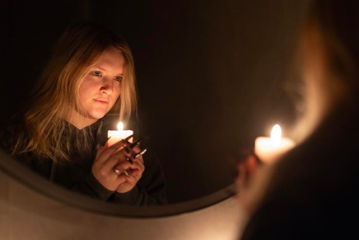 A young woman tenderly holds a lit candle her reflection softly visible in the mirror the warm