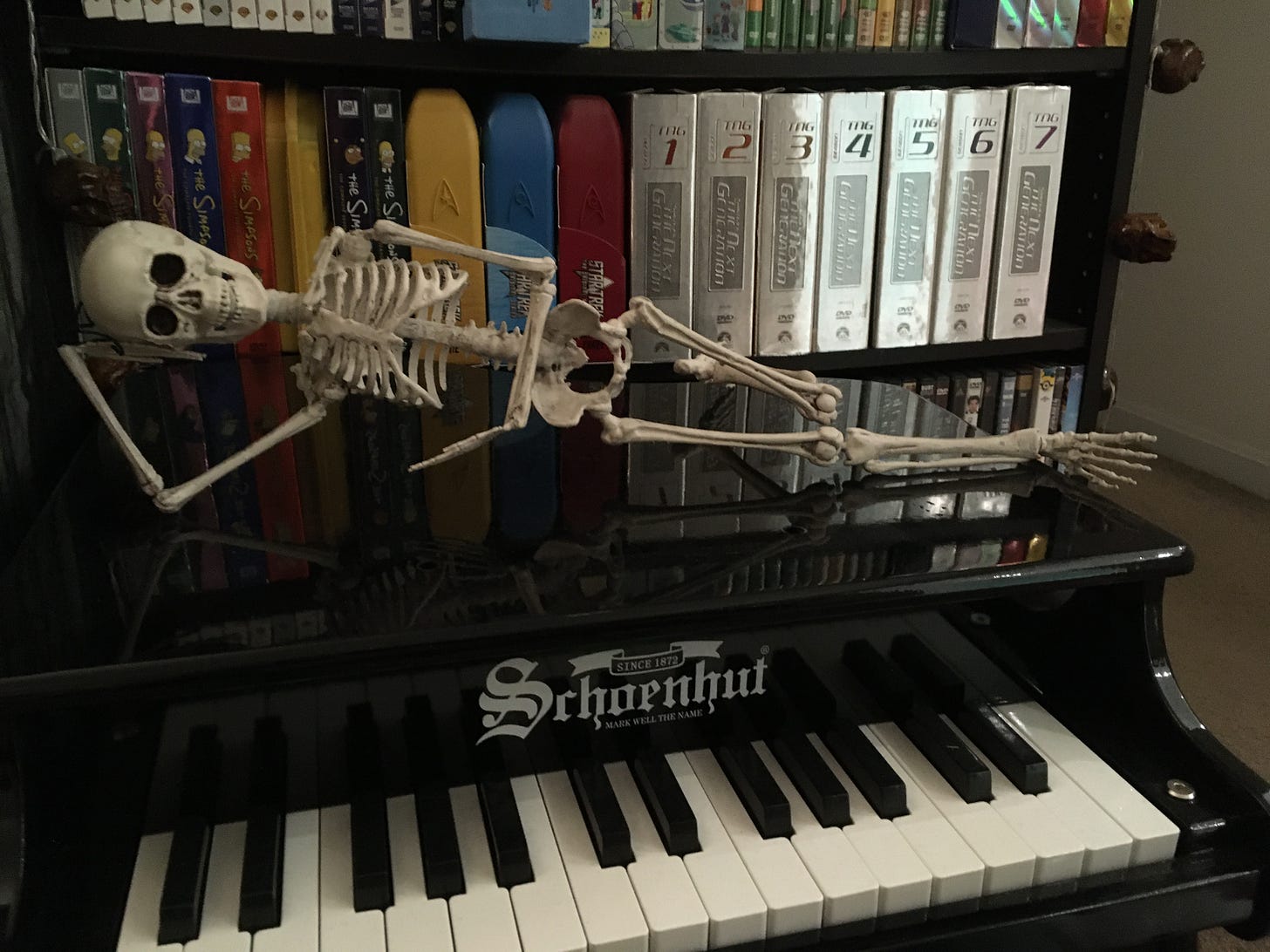 A toy skeleton lying seductively on top of a toy piano