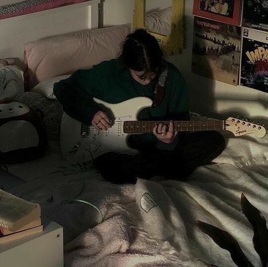 This may contain: a person sitting on a bed playing an electric guitar
