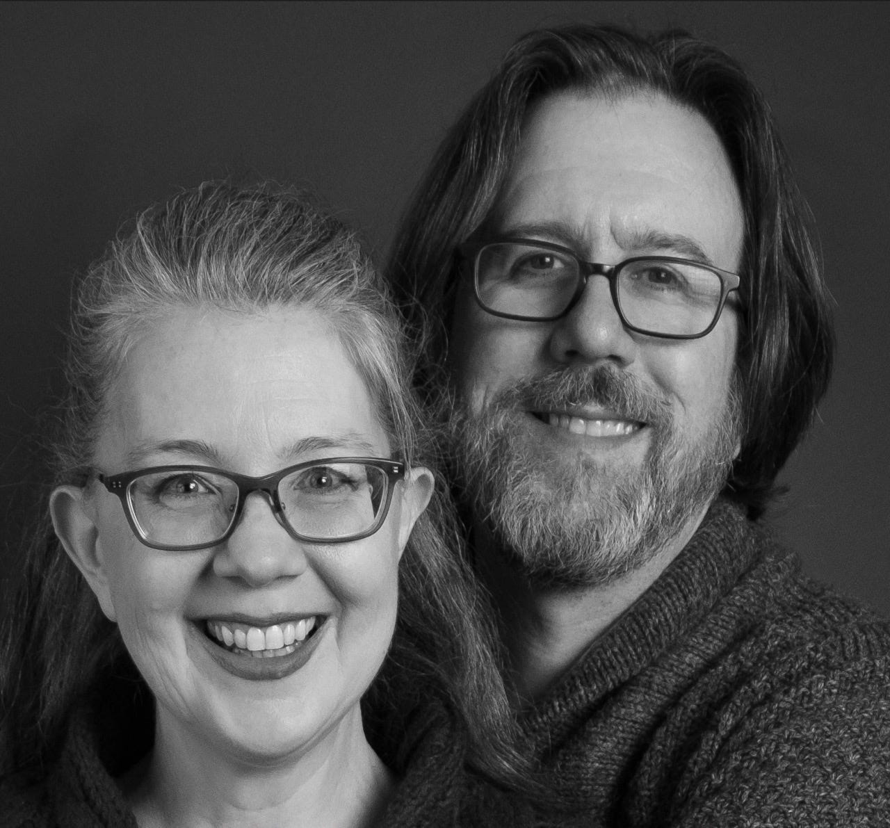 Black and white image of a woman's face and a man's face, both smiling, with the man's face slightly out of focus.