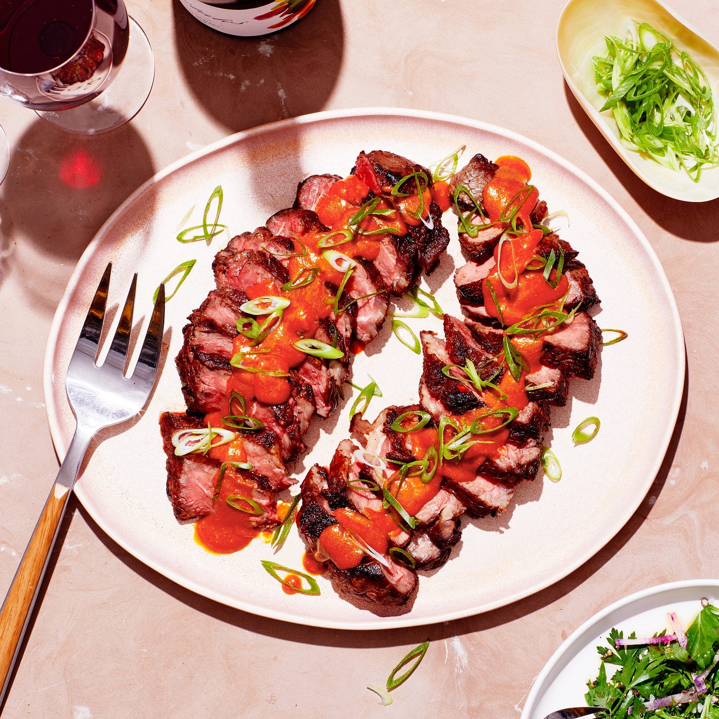 Plate with strips of steak with the butter sauce on top and a side salad on the corner