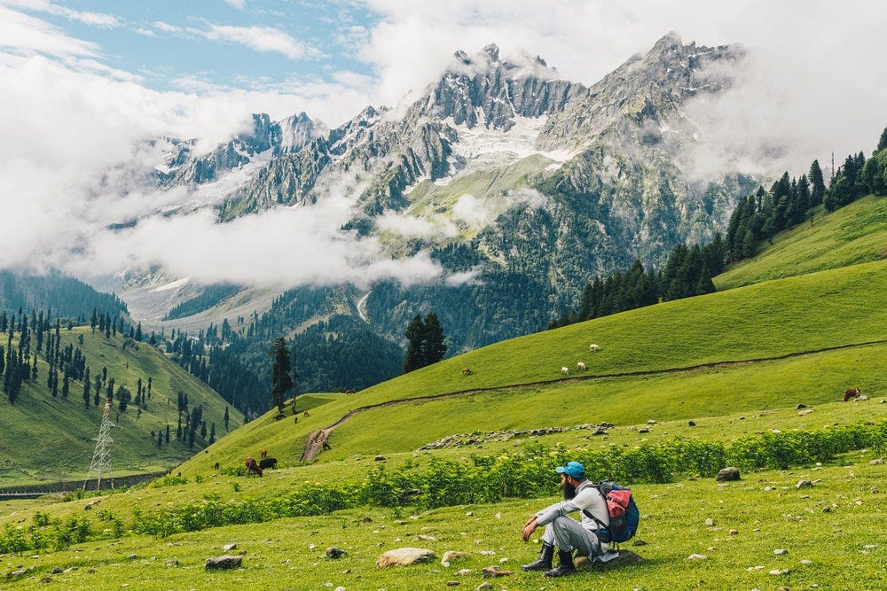 person riding motorcycle on green grass field near snow covered mountain during daytime