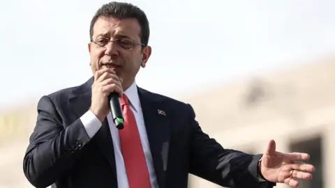 EPA Ekrem Imamoglu, dressed in a suit and red tie, holds a microphone in his right hand and extends his left hand, as he speaks to supporters a day after his university diploma was revoked EPA Ekrem Imamoglu, dressed in a suit and red tie, holds a microphone in his right hand and extends his left hand, as he speaks to supporters a day after his university diploma was revoked