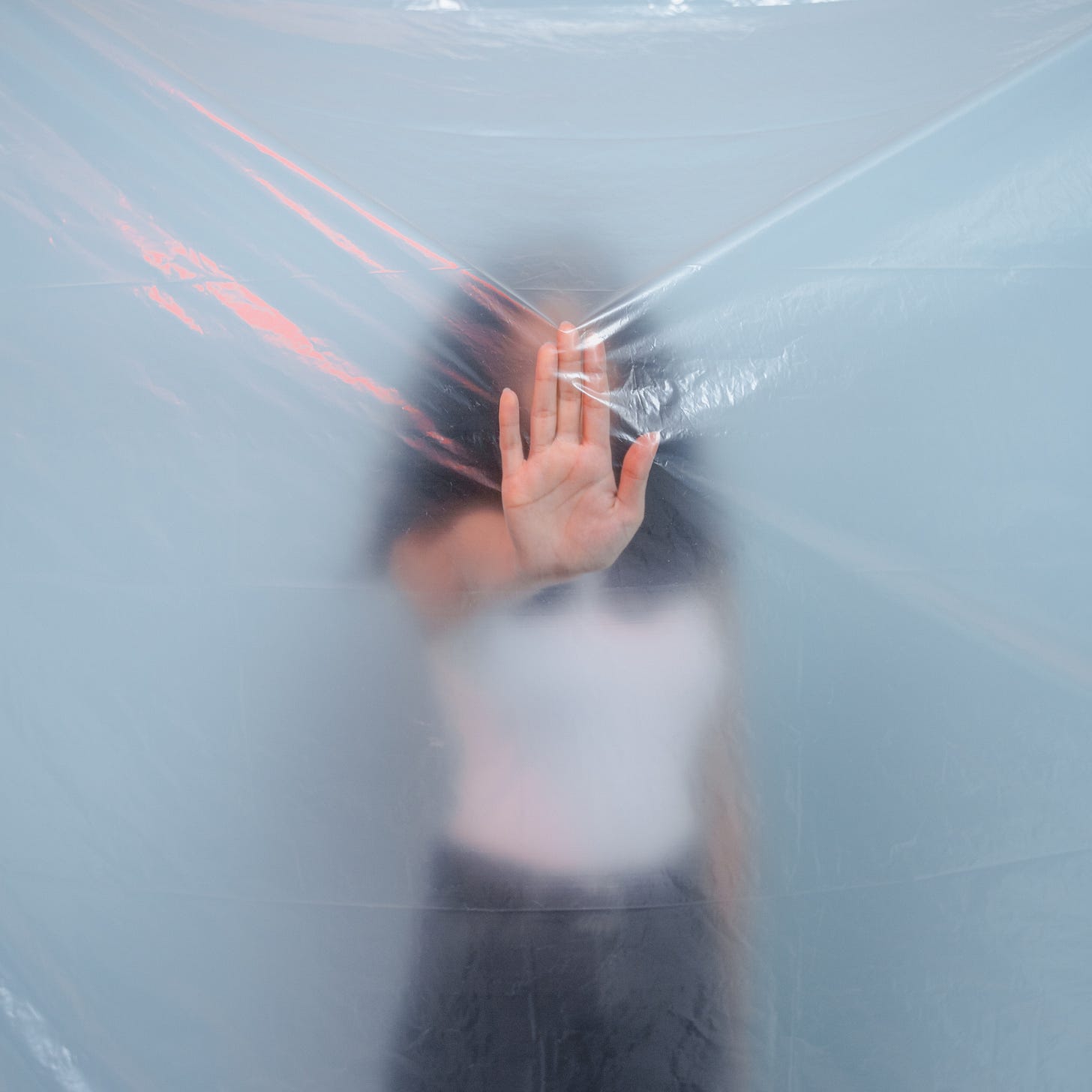 Vrouw achter doorschijnende plastic laag als visuele metafoor voor invisible load, onzichtbaar seksisme en patriarchale werkdruk Vrouw achter doorschijnende plastic laag als visuele metafoor voor invisible load, onzichtbaar seksisme en patriarchale werkdruk