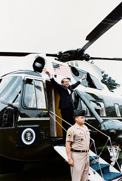 Nixon with arms spread grinning making V sign in front of marine one airplane; a marine stands at bottom of ramp; this was just before Nixon's resignation became effective