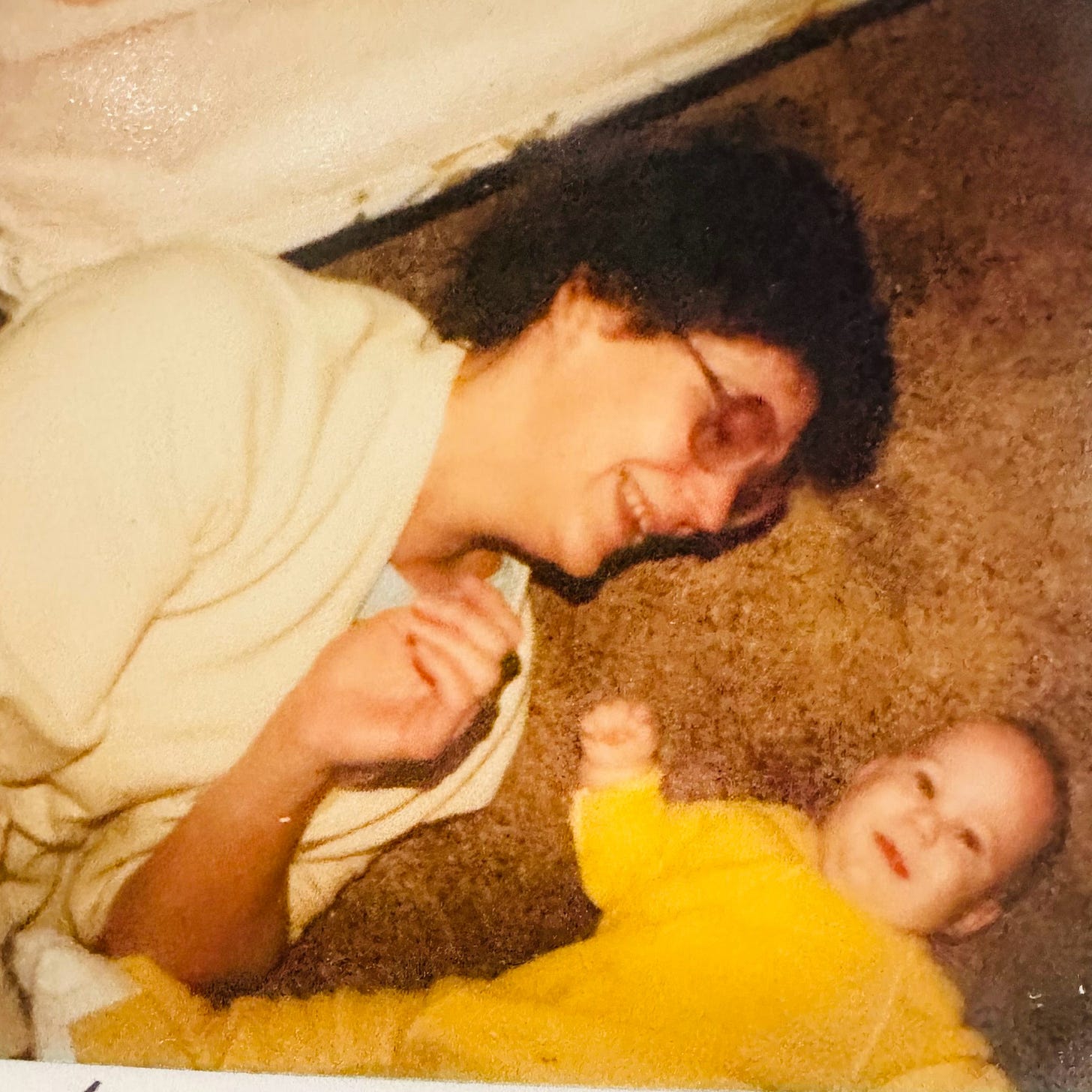 An old family photo showing a mom, laughing, lying on the carpet with her baby, who looks up at the camera An old family photo showing a mom, laughing, lying on the carpet with her baby, who looks up at the camera