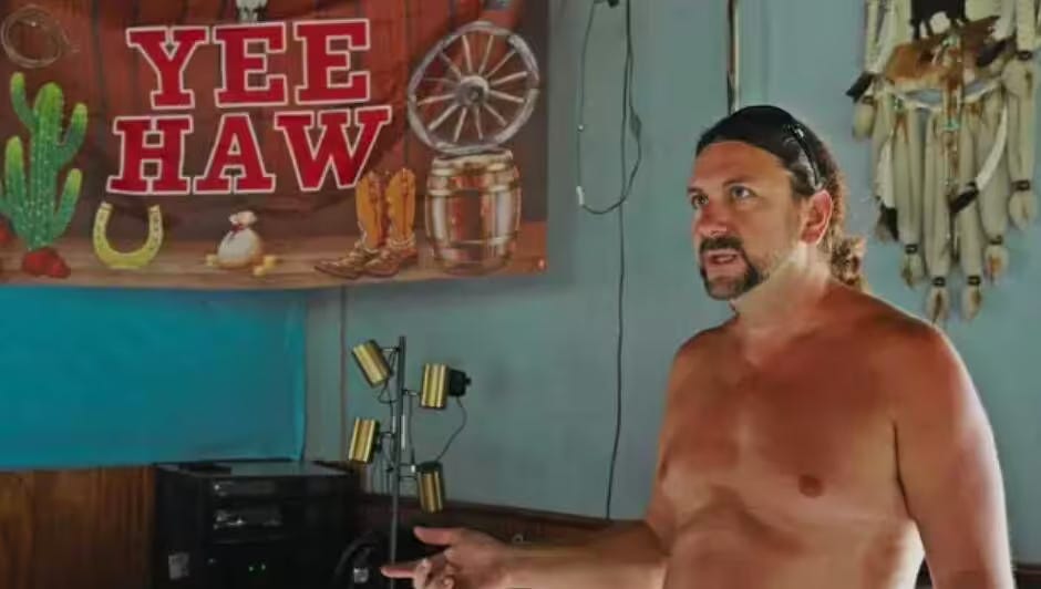 Tim Kraemer, nicknamed “Naked Jesus,” stands nude outdoors at Indian Hills Nudist Park, surrounded by trees and sunlight, smiling confidently toward the camera. Tim Kraemer, nicknamed “Naked Jesus,” stands nude outdoors at Indian Hills Nudist Park, surrounded by trees and sunlight, smiling confidently toward the camera.