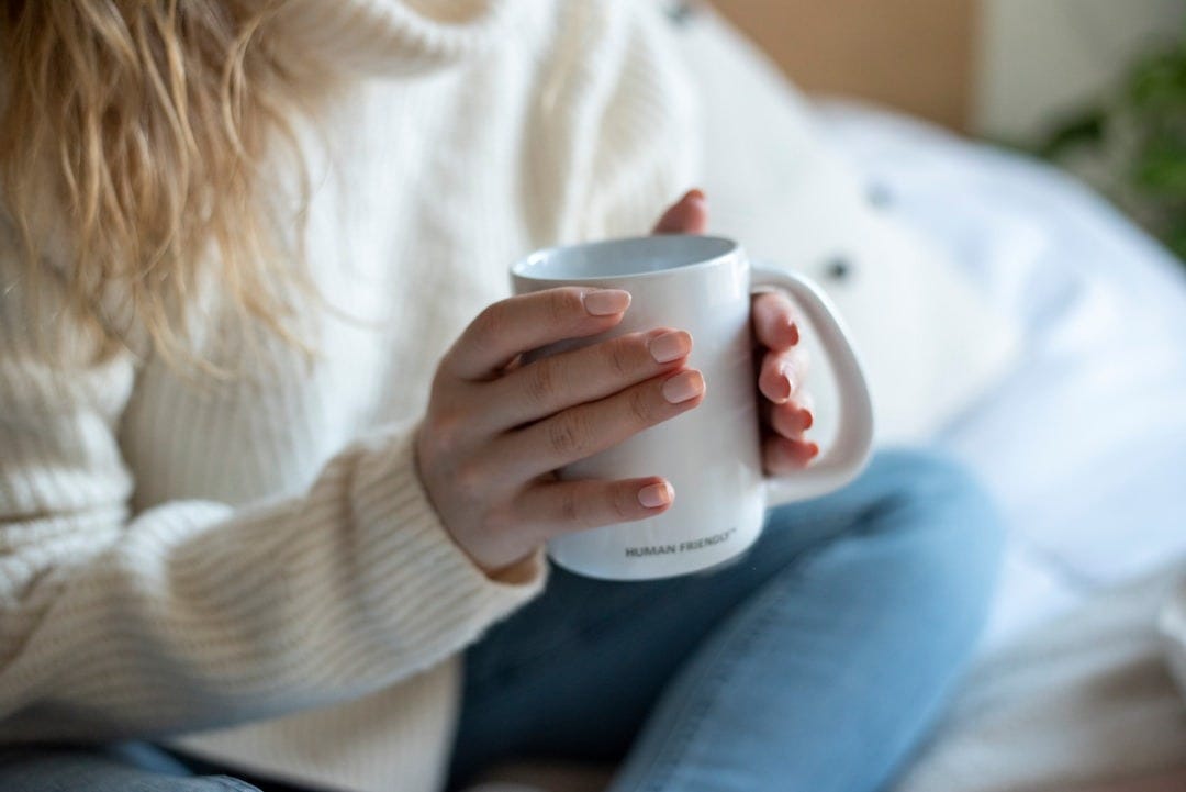 a woman sitting on a bed holding a coffee mug a woman sitting on a bed holding a coffee mug