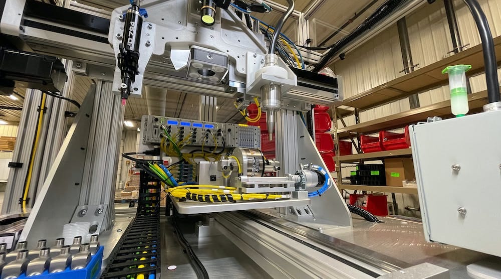 A closeup view of the Y axis, center, and the Z and X axes, above. On the Z axis from left to right are the Nordson adhesive applicator, Banner vision system and plasma gas applicator. The pick-and-place guided actuator is mounted behind the plasma applicator and is not easily distinguished. A box of die-cast housings is visible on the lower left.