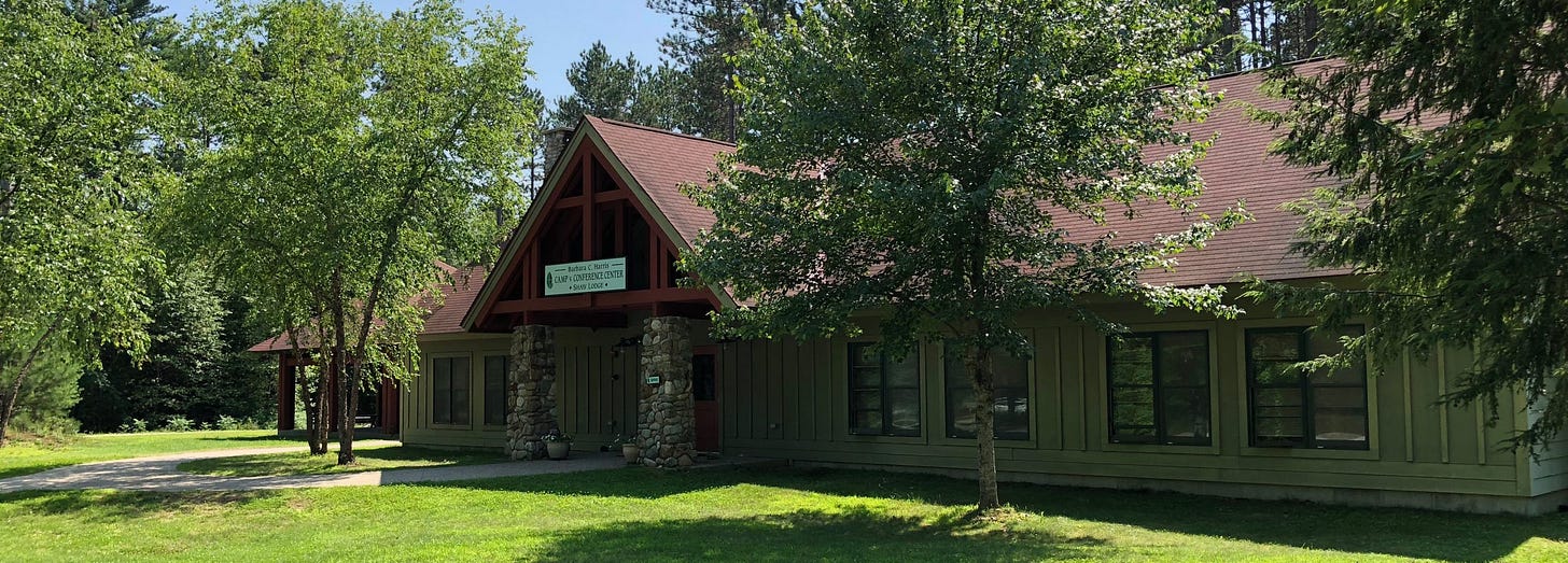 A stone and siding lodge building with a red roof surrounded by green lawns and trees.