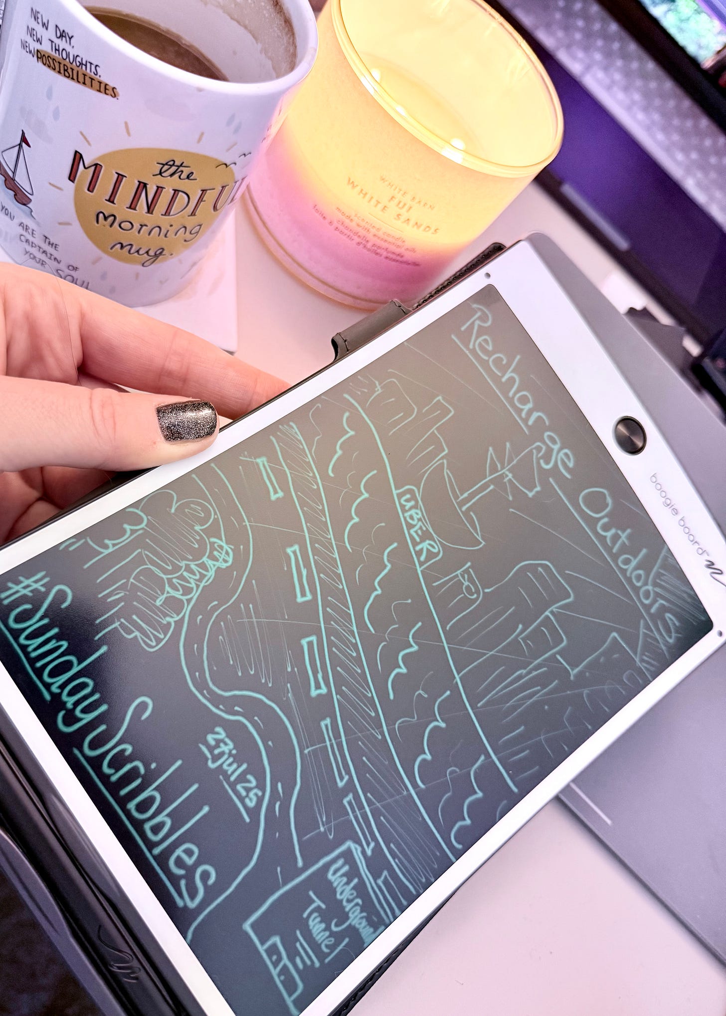 A hand-drawn digital scribble on a Boogie Board tablet. The drawing depicts a winding road leading outdoors, with smaller drawings of an underground tunnel and a car labeled "UBER." The text reads "#SundayScribbles" and "Recharge Outdoors." The tablet is held in front of a coffee mug and a candle.