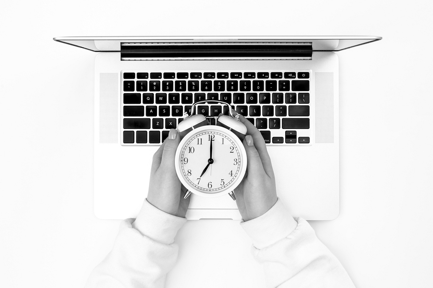 Hands holding a clock over a laptop keyboard.