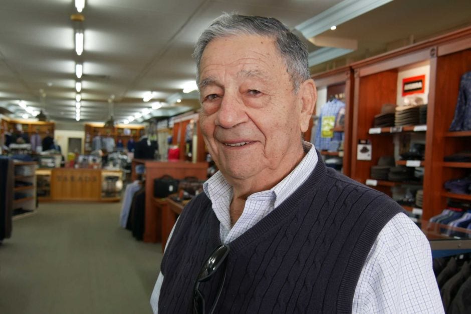 A portrait photo of a man's face, as he stands inside his clothing store, looking out. A portrait photo of a man's face, as he stands inside his clothing store, looking out.