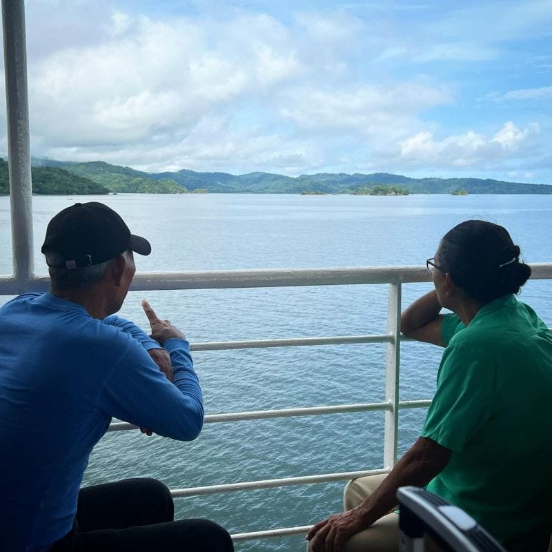 Een ouder stel kijkt uit over zee naar de bergen