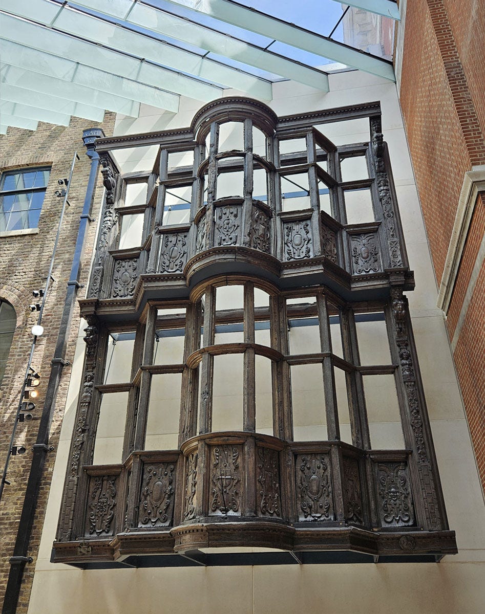 A decoratively carved wooden facade from a two-storey building hanging from a gallery wall A decoratively carved wooden facade from a two-storey building hanging from a gallery wall