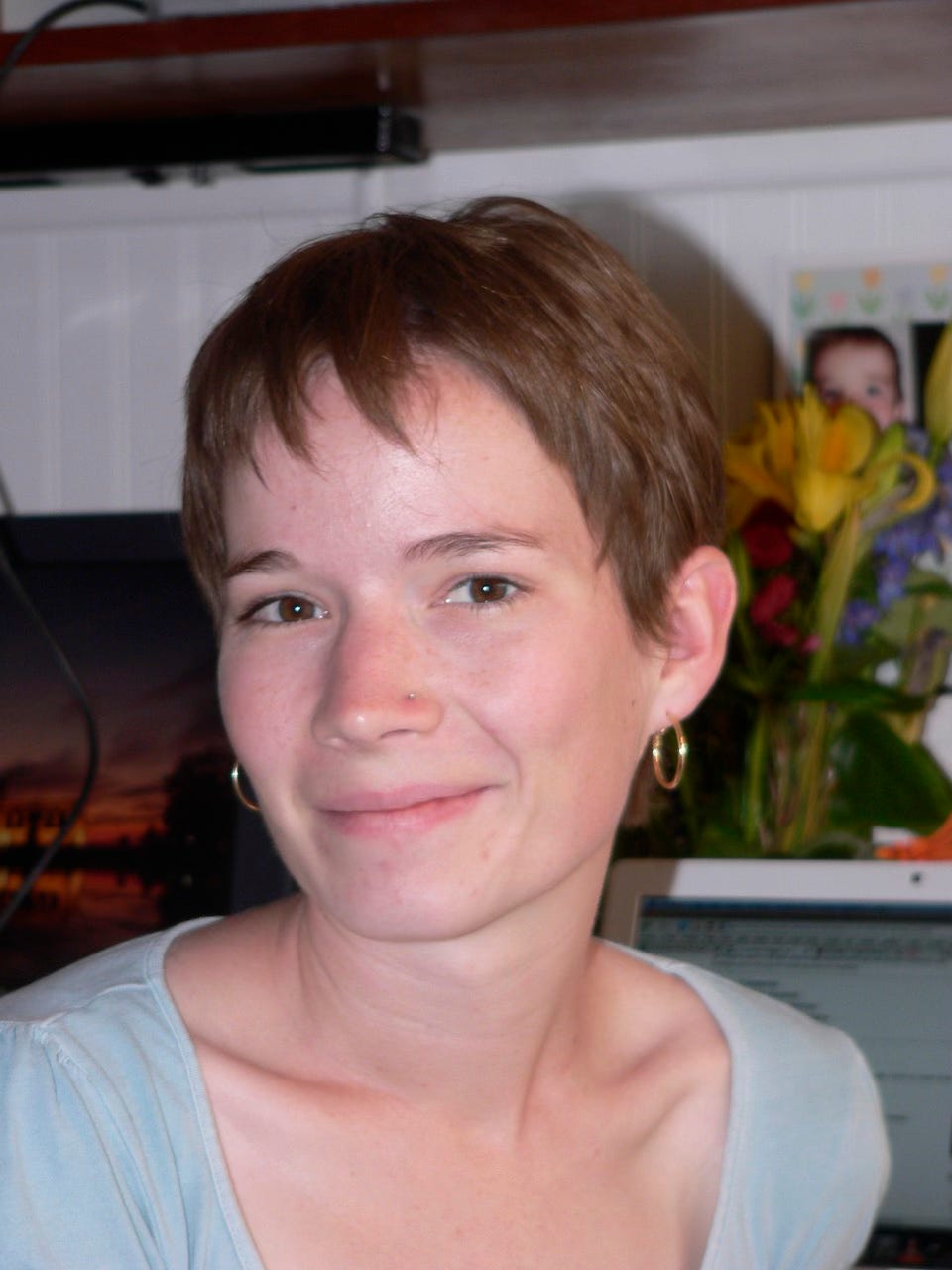 A young woman with a pixie haircut smiles slightly at the camera