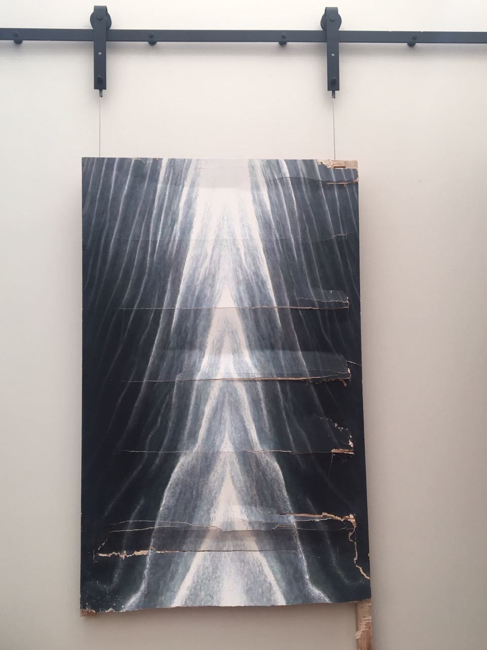 pintura em preto e branco que aparece com a tela rasgada em várias linhas. o quadro está pendurado numa estrutura de ferro, apoiada numa parede branca.