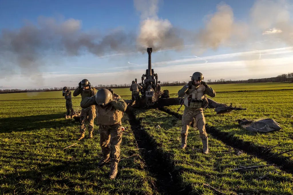 Soldiers in helmets holding their ears as an artillery gun goes off.