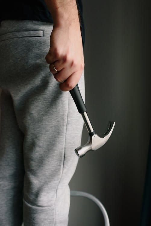 Free Crop unrecognizable male in casual clothes holding metal hammer with rubber handle in room Stock Photo