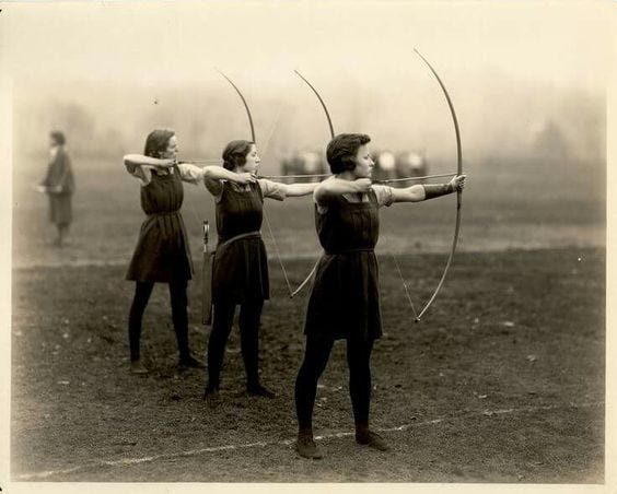 This may contain: three women with bows and arrows in their hands are standing on a field, facing opposite directions
