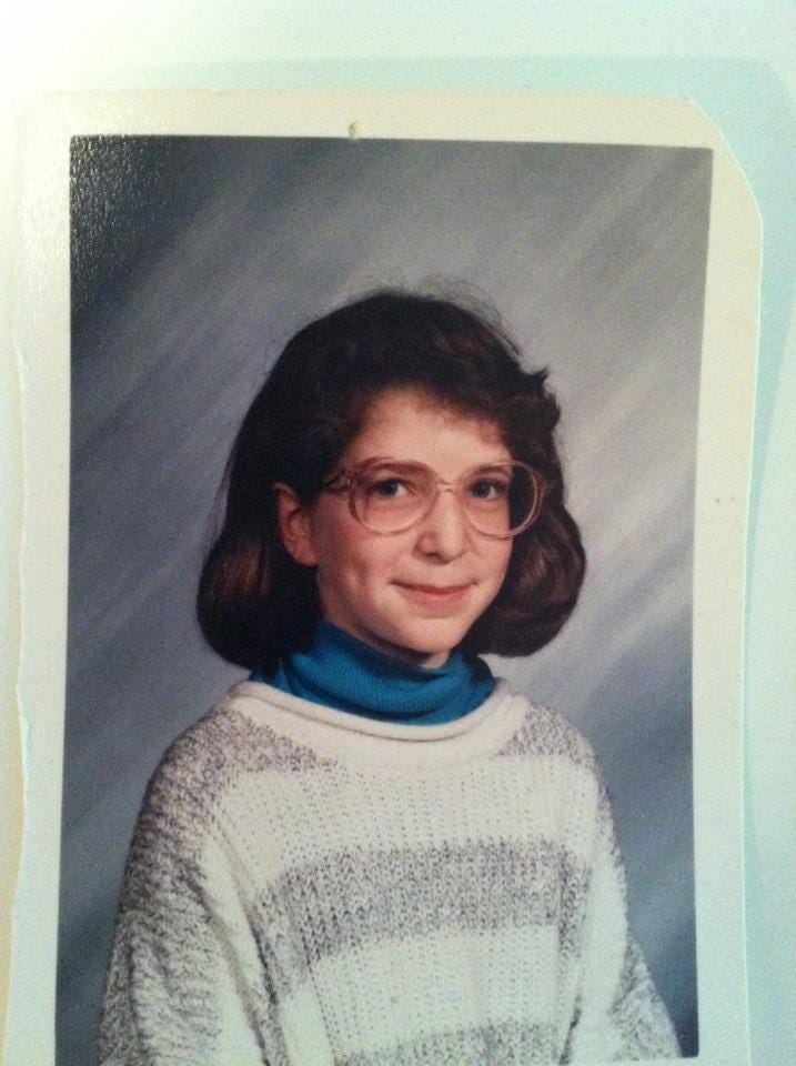 An 11 - year - old girl in 1989, wearing pink glasses and a turtleneck and looking way sassier than she has any right to look.