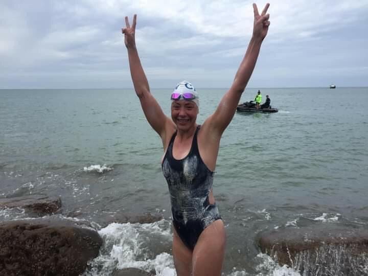 Marion Joffle stands in a swimsuit with the English channel behind her, arms raised in a victory sign Marion Joffle stands in a swimsuit with the English channel behind her, arms raised in a victory sign